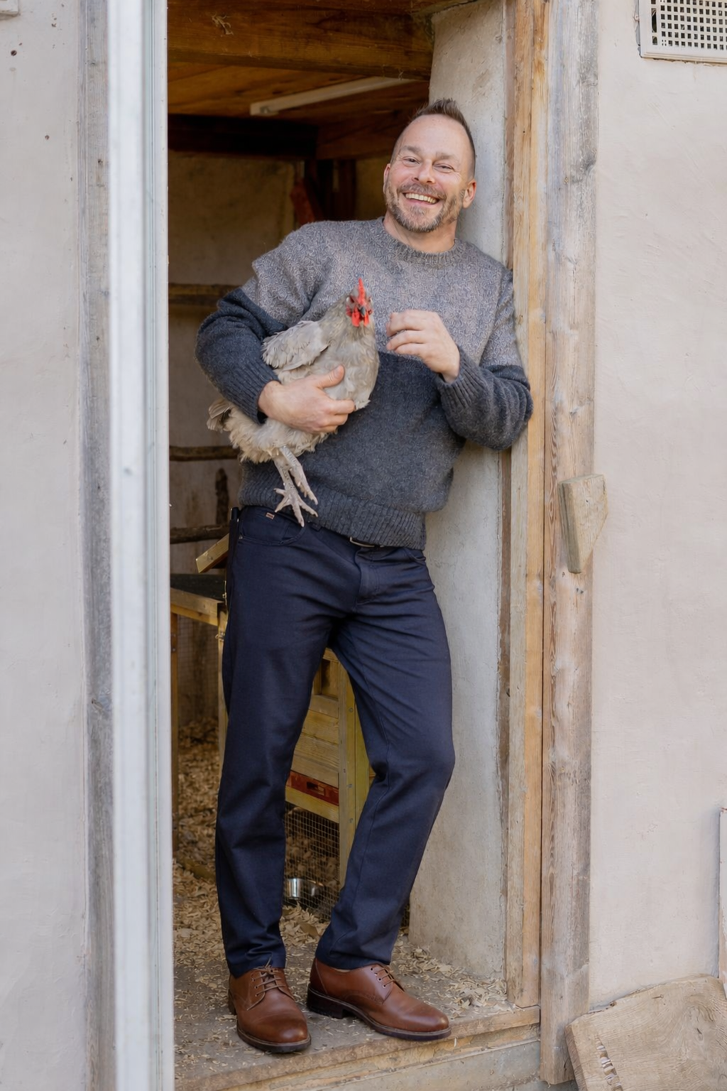 Jake Bergeron holding a chicken in the doorway of his straw bale coop