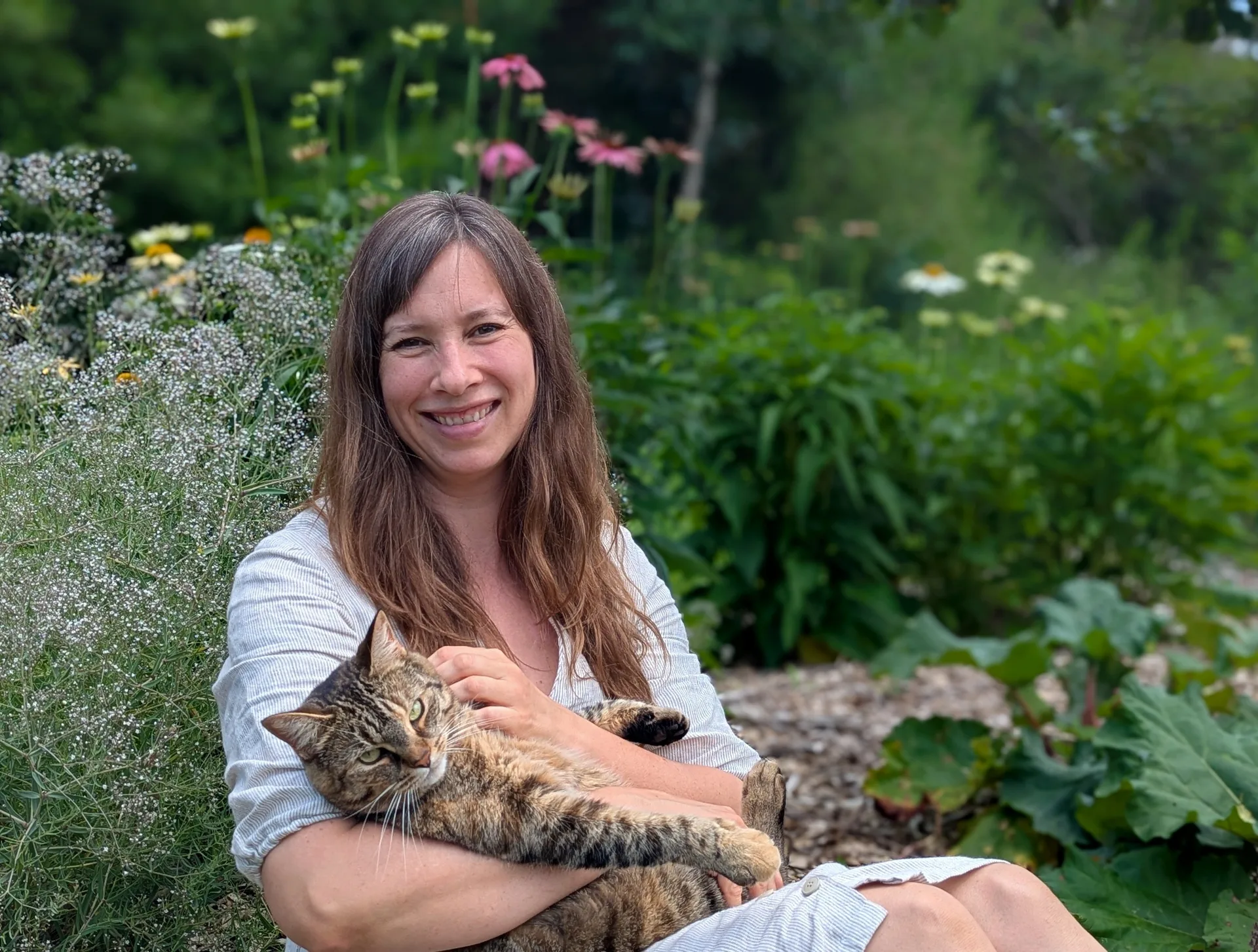 Janna Bergeron in her pollinator garden in Prince Edward County, holding the family cat among coneflowers and baby's breath