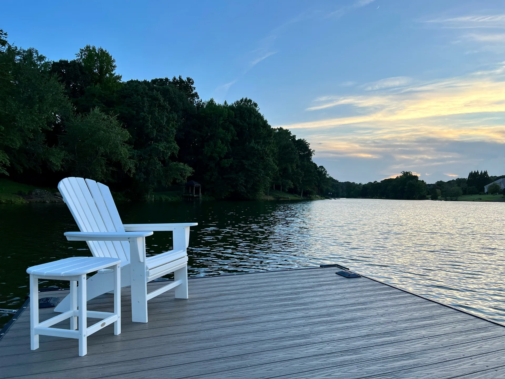 White Adirondack chairs on a dock overlooking a calm Ontario lake at dusk