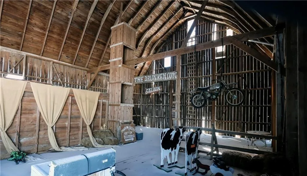 Interior of an old Prince Edward County barn repurposed into a rustic saloon-themed space, with original timber trusses, hanging motorcycle, and hand-painted signage
