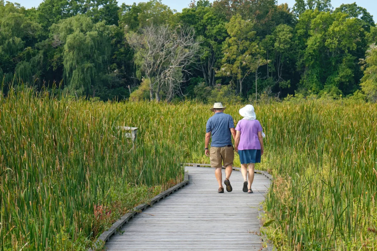 Couple walking hand in hand on a boardwalk through the Ontario countryside — retiring in Prince Edward County