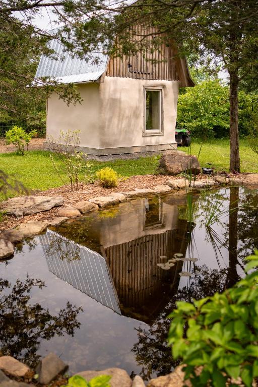 The finished straw bale coop with gambrel metal roof, reflecting in the pond